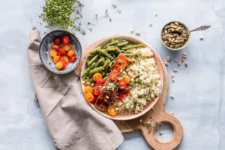 Sund mad serveret på 3 tallerkner: bønner, tomater, laks, couscous og andre grøntsager.